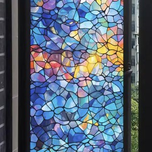 Puede incluir: Una ventana con un diseño de vidriera de colores. El vidrio presenta un patrón de mosaico de azules, morados y amarillos, enmarcado por un borde negro. La ventana está abierta, revelando el exterior.