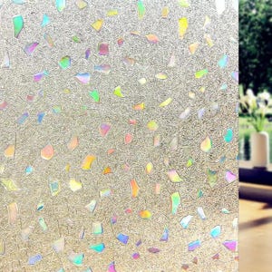 May include: A decorative window film with a textured, iridescent surface. The film is covered with irregularly shaped, colorful, and reflective pieces. The colors include shades of green, yellow, pink, and blue, creating a shimmering effect. The film is designed to be applied to windows.