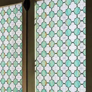 Puede incluir: Ventana decorativa con un patrón repetitivo de cuadrifolios blancos sobre un fondo turquesa y óxido. La ventana está enmarcada en verde claro, con un tirador negro visible.