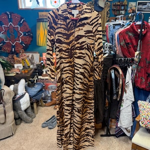 May include: A long-sleeved, floor-length robe featuring a brown and tan tiger stripe pattern. The garment has a full-length front zipper closure, a fold-over collar, and is constructed from a soft, textured fleece-like material.