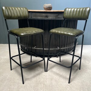 May include: Two green leather bar stools with black metal frames. The stools have a tufted back and seat.