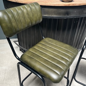 May include: Two green leather bar stools with black metal frames. The stools have a tufted backrest and a padded seat.