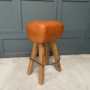 May include: A brown leather bar stool with a wooden frame and a metal footrest. The stool has a unique, quilted design on the seat.