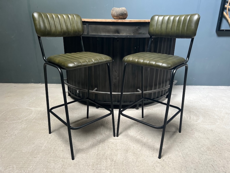 May include: Two green leather bar stools with black metal frames. The stools have a tufted back and seat.