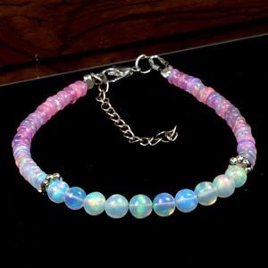 May include: A delicate bracelet featuring iridescent opal beads and smaller pink and purple beads. The bracelet has a silver-colored chain and clasp, and is approximately 7 inches (17.78 cm) in length.