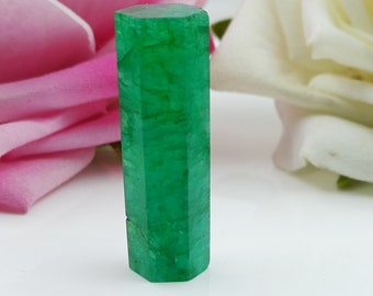 May include: A deep green emerald gemstone, cut into a hexagonal prism shape. It measures 10 x 37 mm and weighs 45 carats.