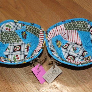 May include: Two blue fabric bowls with a patchwork design featuring cherries, bees, and a honeycomb pattern. The bowls are handmade and have a rustic charm.