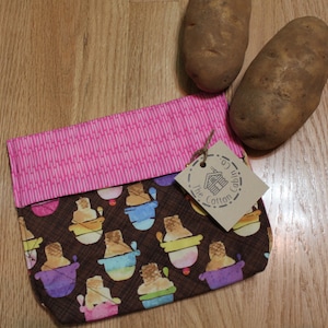 Könnte beinhalten: Eine braune gesteppte Reißverschlusstasche mit einer rosafarbenen Stoffklappe. Die Tasche hat ein sich wiederholendes Muster aus bunten Eiswaffeln auf braunem Hintergrund. Ein braunes Etikett mit dem Text "The Cotton Cabin" ist an der Tasche befestigt.