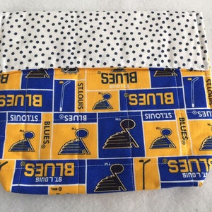 Könnte beinhalten: Eine blaue und gelbe gesteppte Stofftasche mit dem St. Louis Blues Logo, das auf der Vorderseite wiederholt wird. Die Tasche hat ein weißes Futter mit Punkten.