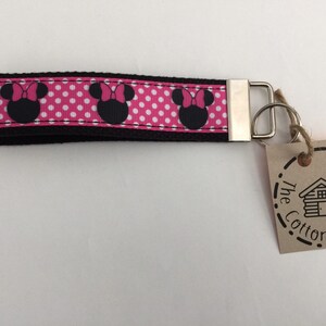 May include: Pink and black polka dot key chain with three black Minnie Mouse heads. The key chain has a silver key ring and a brown tag with the text "The Cotton Cabin Co."