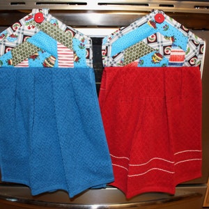 May include: Two oven mitts hanging on a silver oven door. The mitts are made of red and blue fabric with a patchwork design. The patchwork design features a variety of fabrics with different patterns, including plaid, polka dots, and floral prints.