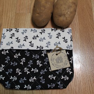 Könnte beinhalten: Eine schwarze und weiße Stofftasche mit einem Fischgrätenmuster. Die Tasche ist in der Mitte gefaltet und hat ein braunes Etikett mit der Aufschrift "The Cotton Cabin Co."