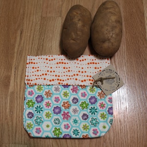 Könnte beinhalten: Eine kleine, wiederverwendbare Stofftasche mit weißem Hintergrund und einem bunten Blumenmuster. Die Tasche ist gefaltet und hat ein Etikett mit der Aufschrift "The Cotton Co."