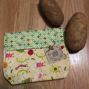 Könnte beinhalten: Eine gelbe Stofftasche mit einem grün-braunen Muster oben. Die Tasche hat ein gestepptes Design und zeigt einen Cartoon-Druck mit verschiedenen Früchten und Gemüse. Ein braunes Etikett mit dem Text "The Cotton Cabin Co." ist an der Tasche befestigt.