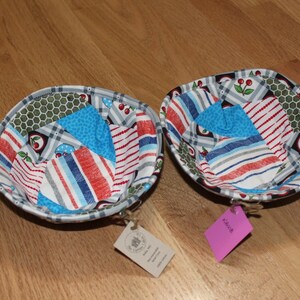 May include: Two fabric bowls with a patchwork design featuring red, white, blue, and green fabric. The bowls are lined with a white fabric and have a cherry design.