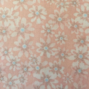 May include: A close-up of a peach-colored fabric with a white floral pattern. The flowers have a light blue center.