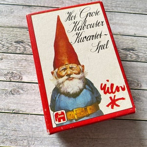 以下が含まれることがあります： 赤い箱に白い背景、赤い帽子と青いズボンを着た漫画のノームが描かれています。箱には「Het Grote Kabouter Kwartet - Spel」と書かれており、小さな象のロゴには「Jumbo」と書いてあります。