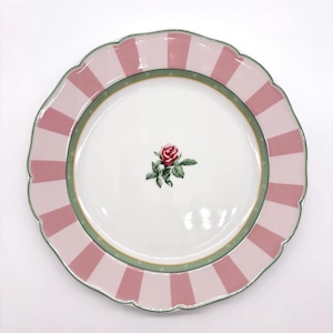 May include: A round ceramic dinner plate with a scalloped edge, featuring a white center with a single red rose and green leaves. The rim is decorated with alternating light and dark pink vertical stripes, bordered by a thin green and gold trim.