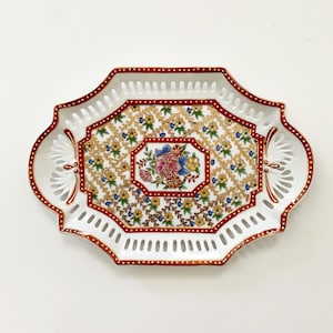 May include: A white porcelain serving tray with a red and gold border and a floral design in the center. The tray has a scalloped edge and a cut-out design around the border.