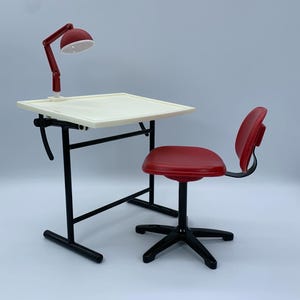 May include: A miniature drafting table set with a red adjustable lamp, a cream-colored tabletop, and a red chair. The table has a black frame and a lever for adjusting the angle. The chair has a black base with five legs.