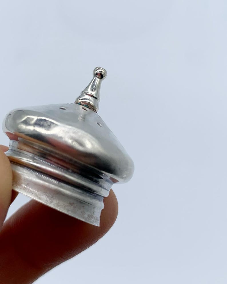 May include: Silver-toned metal bottle stopper with a pointed top and a round base. The stopper has a textured surface and several small holes.