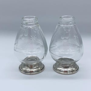 May include: A set of two clear glass salt and pepper shakers with etched floral designs and silver bases.