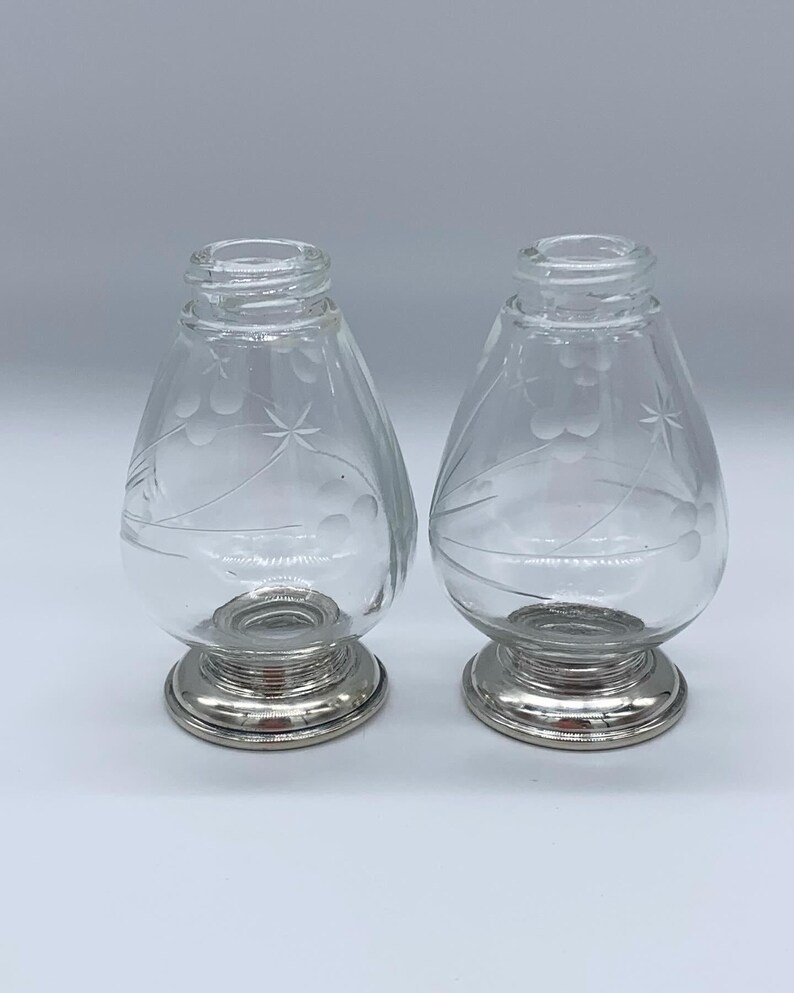 May include: A set of two clear glass salt and pepper shakers with etched floral designs and silver bases.
