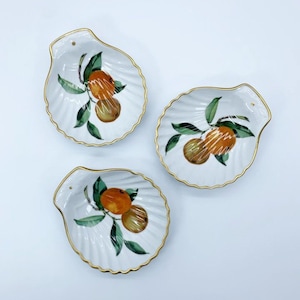May include: Three white, shell-shaped dishes with gold rims. Each dish features a hand-painted design of oranges and green leaves. The dishes are arranged on a white surface, showcasing their decorative appeal.