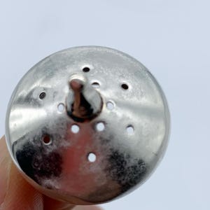 May include: A silver metal bottle stopper with a round top and a pointed tip. The top has multiple small holes.