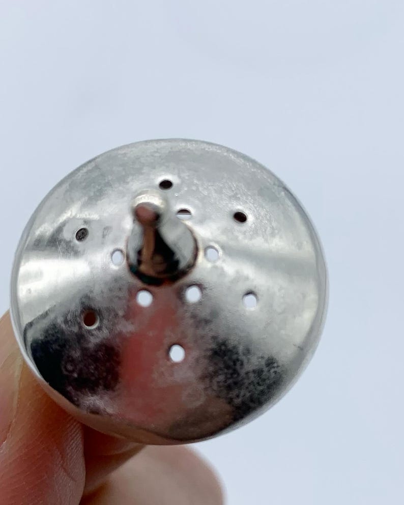 May include: A silver metal bottle stopper with a round top and a pointed tip. The top has multiple small holes.