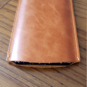 May include: A brown leather phone case with a stitched edge.