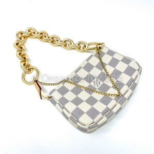 Puede incluir: Un bolso de mano Louis Vuitton a cuadros blancos y grises con una correa de cadena dorada. El bolso tiene una forma peque&ntilde;a y rectangular y un cierre de cremallera.