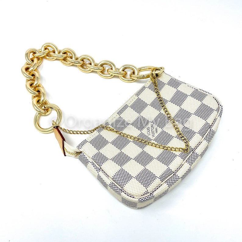 Puede incluir: Un bolso de mano Louis Vuitton a cuadros blancos y grises con una correa de cadena dorada. El bolso tiene una forma peque&ntilde;a y rectangular y un cierre de cremallera.