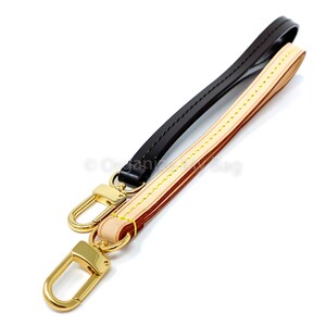 Op de afbeelding: Een bruin leren band met een gouden metalen haak, en een beige leren band met een gele stikseldetail en een gouden metalen haak.