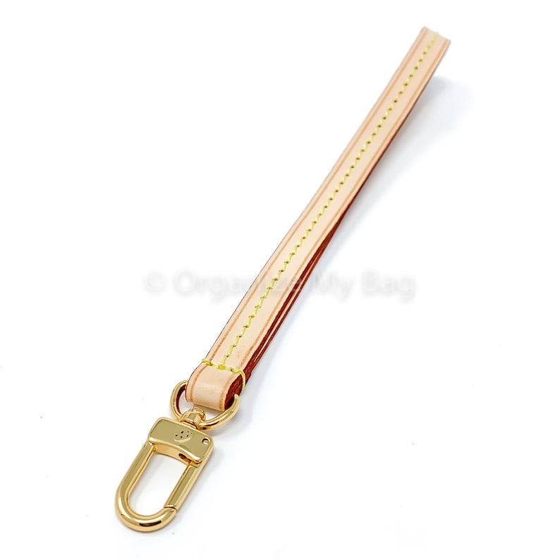 Op de afbeelding: Een lichtbruine leren riem met gele stiksels en een gouden metalen haak. De riem is ongeveer 30 cm lang.