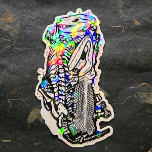 Puede incluir: Pegatina holográfica que presenta un esqueleto de dinosaurio estilizado con una cabeza y acentos de color arcoíris. El diseño incluye estructuras óseas detalladas y un acabado iridiscente texturizado, creando un efecto vibrante. La pegatina está troquelada con un borde blanco.