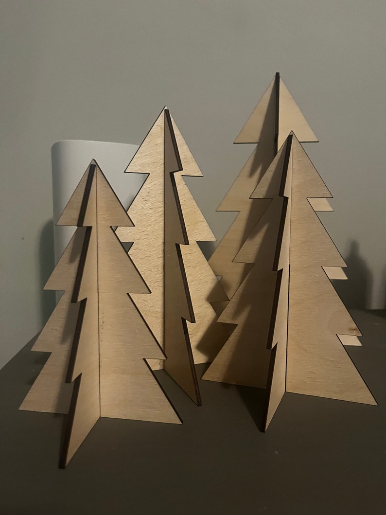 Puede incluir: Cuatro adornos de &aacute;rbol de Navidad de madera en varios tama&ntilde;os. Los &aacute;rboles est&aacute;n hechos de madera marr&oacute;n claro y tienen un dise&ntilde;o simple y minimalista.