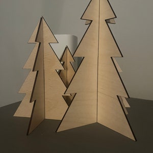 Puede incluir: Tres &aacute;rboles de Navidad de madera de diferentes tama&ntilde;os, de pie sobre una superficie gris oscuro. Los &aacute;rboles est&aacute;n hechos de madera contrachapada y tienen un acabado de madera natural.
