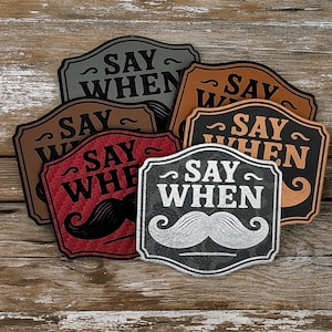 May include: A collection of six decorative signs with the phrase "SAY WHEN" in various colors, including black, brown, red, and gray. Each sign features a mustache graphic and a decorative border, set against a rustic wooden background.