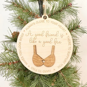 May include: A round wooden ornament with a brown bra cutout and the text "A good friend is like a good bra - Always close to your heart - There to support you - Hard to find - Makes you look good".