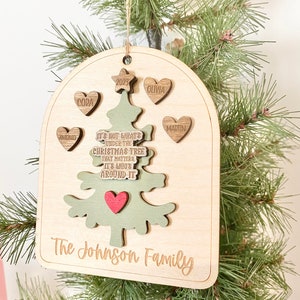 Peut inclure: Une d&eacute;coration de No&euml;l en bois en forme d'arbre avec le texte "Ce n'est pas ce qui se trouve sous le sapin de No&euml;l qui compte, mais qui est autour." L'ornement comporte &eacute;galement une &eacute;toile, des c&oelig;urs avec des noms et l'ann&eacute;e 2023. Le bas de l'ornement porte l'inscription "The Johnson Family".