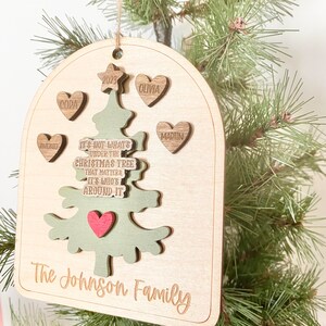 Peut inclure: Une d&eacute;coration de No&euml;l en bois en forme d'arbre avec le texte "Ce n'est pas ce qui se trouve sous le sapin de No&euml;l qui compte, mais qui est autour." et les noms "Antonio", "Cora", "Olivia", "Martin" et "The Johnson Family".