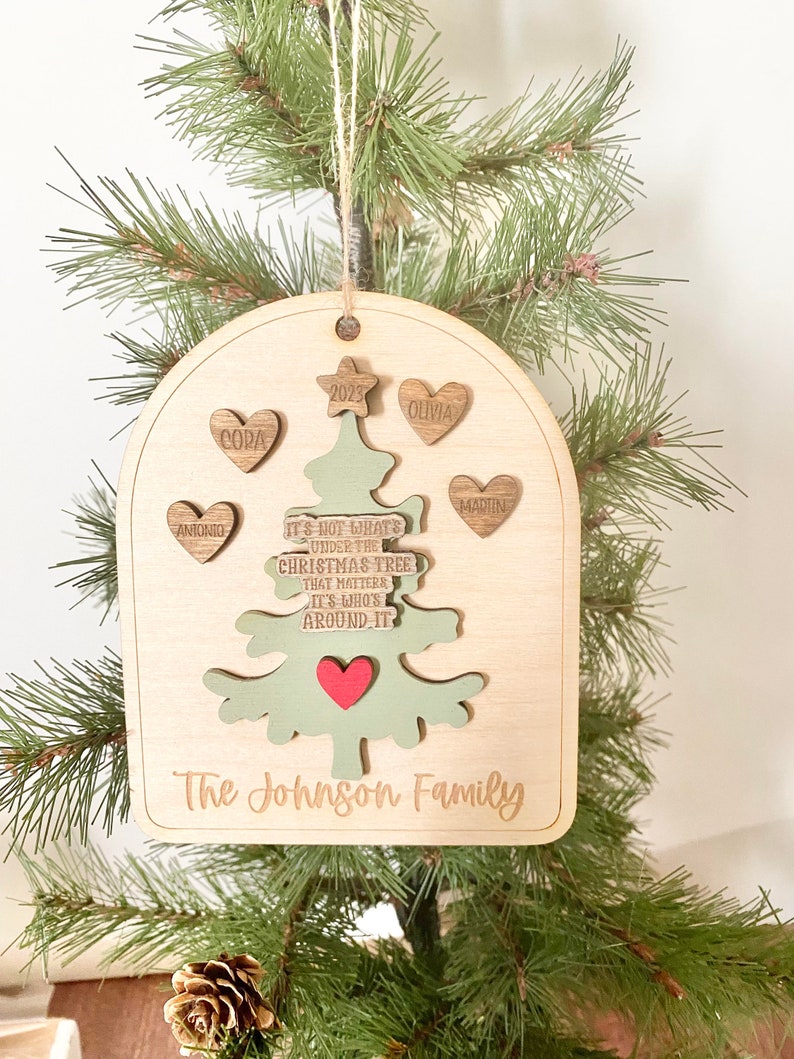 Peut inclure: Une d&eacute;coration de No&euml;l en bois en forme d'arbre de No&euml;l vert avec un c&oelig;ur rouge. L'ornement est personnalis&eacute; avec les noms Antonio, Cora, Olivia, Martin et le texte "Ce n'est pas ce qui se trouve sous le sapin de No&euml;l qui compte, mais qui est autour de lui." L'ornement comprend &eacute;galement l'ann&eacute;e 2023 et le texte "The Johnson Family."