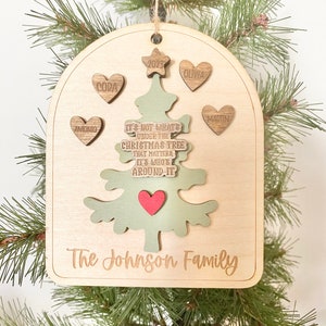 Peut inclure: Une d&eacute;coration de No&euml;l en bois en forme d'arbre avec le texte "Ce n'est pas ce qui se trouve sous le sapin de No&euml;l qui compte, mais qui est autour." L'ornement porte &eacute;galement les noms "Antonio", "Cora", "Olivia", "Martin" et "The Johnson Family".