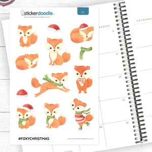 May include: A sheet of stickers featuring watercolour illustrations of foxes wearing winter accessories, such as scarves, hats, and mittens. The stickers are designed for use in planners and journals. The text "#FOXYCHRISTMAS" is printed at the bottom of the sheet.