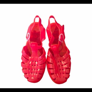 May include: A pair of bright pink jelly sandals with a woven design and a buckle closure.