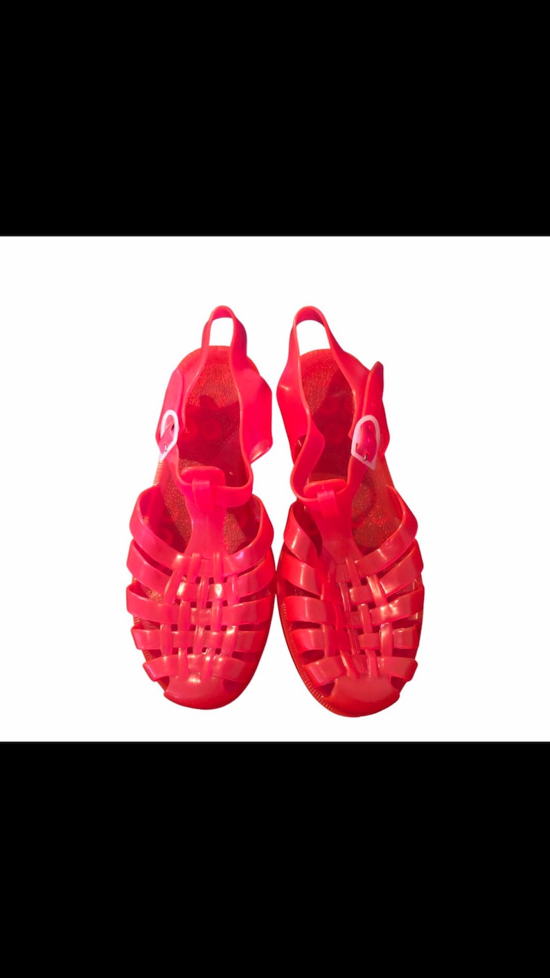 May include: A pair of bright pink jelly sandals with a woven design and a buckle closure.