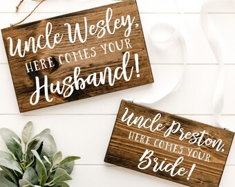 May include: Two rustic wooden signs with white lettering. The top sign reads "Uncle Wesley. Here comes your Husband!" The bottom sign reads "Uncle Preston. Here comes your Bride!"