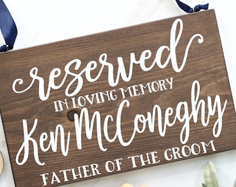 May include: A wooden sign with the text "reserved in loving memory Ken McConeghy father of the groom" in white lettering.