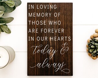 May include: A dark brown wooden sign with white text that reads "In loving memory of those who are forever in our hearts today & always".